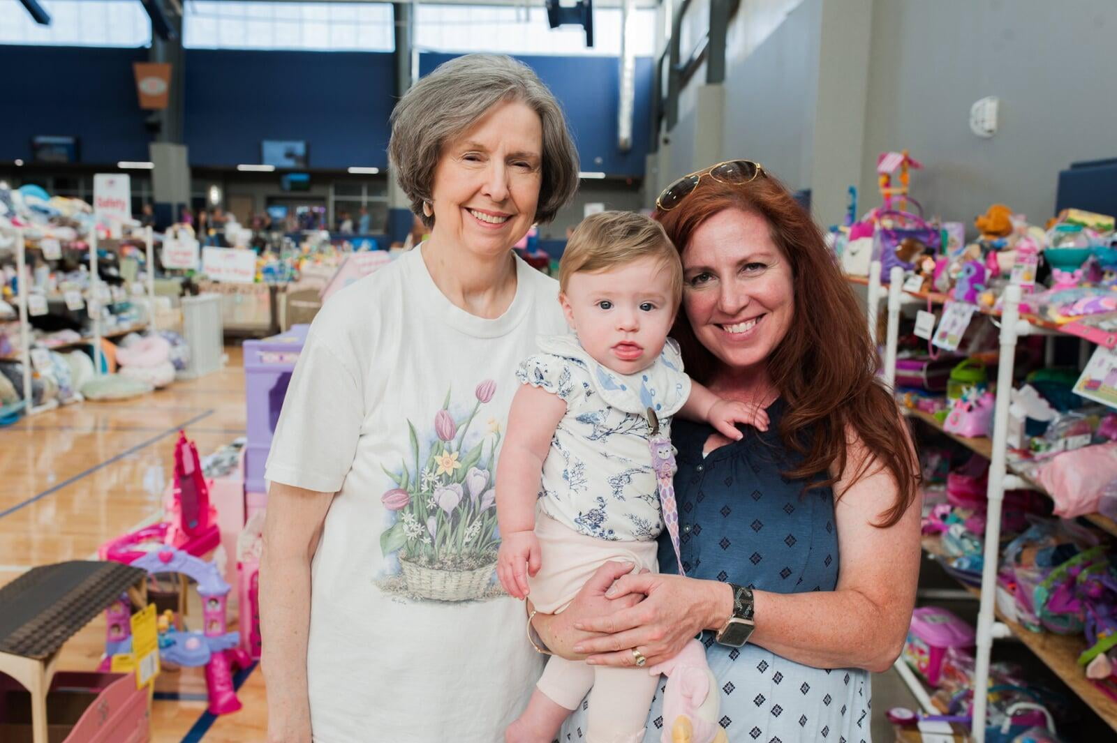 A mom, abuela and granddaughter attend a JBF sale in Dallas. Abuela is holding a babyseat.
