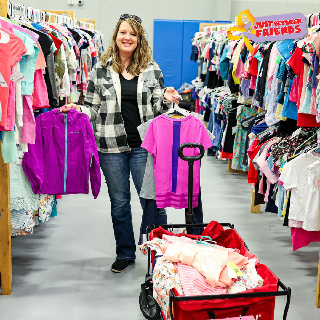 Beautiful mom holds two boys tops—one in each hand—as she shops the deals at her local sale.